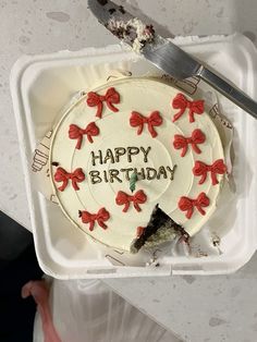 a birthday cake with red bows on it in a plastic container next to a knife