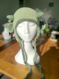 a white mannequin head wearing a green crocheted hat with horns and ears