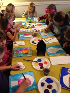 children are sitting at a table painting with watercolors and paper plates on it