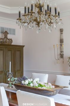 a chandelier hangs above a dining room table with flowers on it and candles in the center