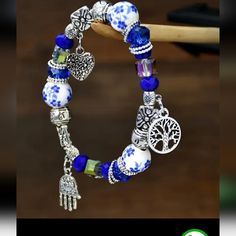 This Beautiful Bracelet Features Bright Blue & White Porcelain Ceramic Beads, Clear And Royal Blue Crystal Beads And Has Silvertone Beads And Spacers. The Three Silvertone Charms - A Heart, A Hand And A Tree Of Life - Give This Bracelet A Unique Look That Will Bring Many Compliments Your Way. The Bracelet Measures 2.5" Across And The Stretchy Elastic Ensures A Snug, Comfortable Fit. Nwt Porcelain Bead Bracelet, Porcelain Beads Jewelry, Artisan Blue Bracelets Collectible, Bohemian Blue Charm Bracelet With Colorful Beads, Spiritual Blue Hand-strung Bracelets, Ceramic Beads, Porcelain Ceramics, Blue Crystals, White Porcelain