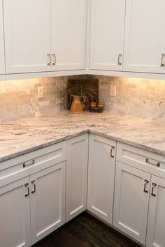 a kitchen with white cabinets and marble counter tops