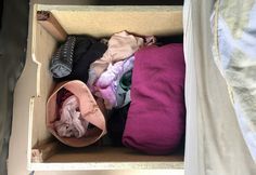 an open cardboard box filled with clothes on top of a bed