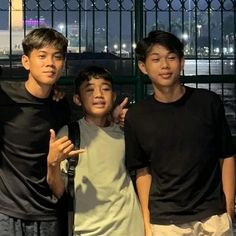 three young men standing next to each other in front of a metal fence and gate