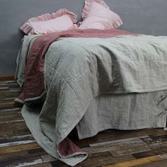 the bed is made up with pink and grey linens on it, along with two pillows