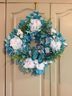 a blue and white wreath hanging on the front door with butterflies around it, surrounded by greenery