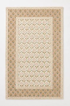 a beige and green rug with an intricate design on the bottom, in front of a white wall