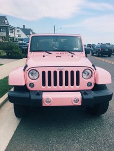 a pink jeep is parked on the side of the road in front of some houses