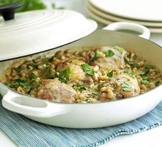 a white casserole dish filled with meat and beans, garnished with parsley