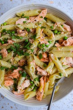 a white bowl filled with pasta and salmon on top of a table next to a fork