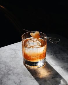 an old fashioned cocktail with ice and orange peel on the rim, sitting on a marble table