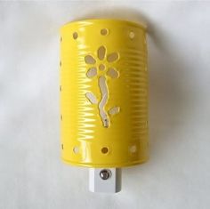 a yellow cup with holes on it sitting on a white wall next to a light switch