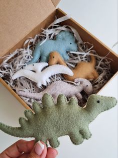 a hand holding a small dinosaur ornament in a box with other toy dinosaurs