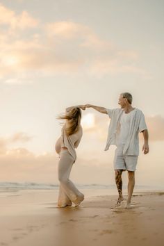 a pregnant woman dancing on the beach with her husband, who is holding his hand