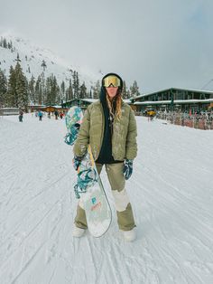 a woman holding a snowboard on top of a snow covered slope