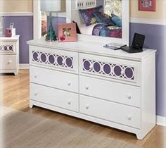 a white dresser with drawers and a mirror on top of it in front of a purple wall