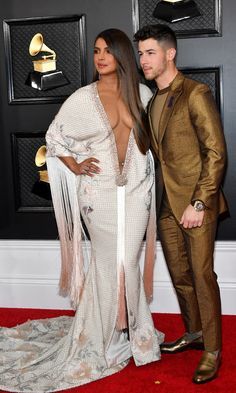 two people standing next to each other on a red carpet with one person wearing a gold suit