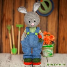 a knitted bunny is standing in front of some flowers and gardening tools on a table