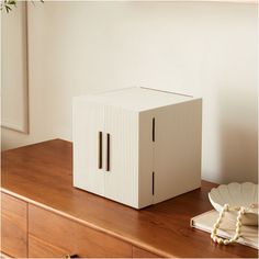 a white box sitting on top of a wooden table next to a plate and vase