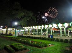 fireworks are lit up in the night sky above an open area with benches and tables