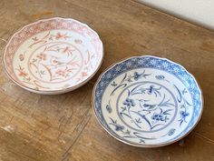 two blue and white plates sitting on top of a wooden table next to each other