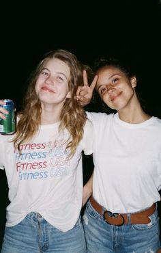 two young women standing next to each other holding up peace signs and drinking sodas