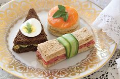 a plate topped with sandwiches and cucumbers on top of a lace table cloth