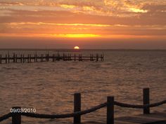 the sun is setting over the ocean with a dock in the foreground