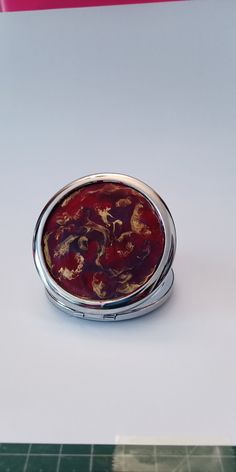 a compact mirror sitting on top of a white table next to a pink and red object