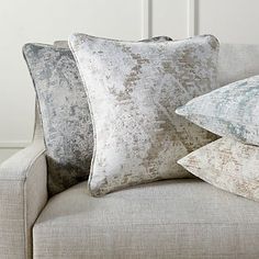 three pillows are stacked on top of each other in front of a beige couch with white walls