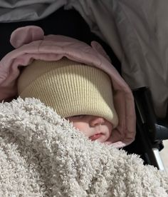 a baby sleeping in a stroller wearing a pink hat and blanket on top of it's head