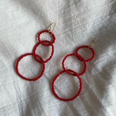 three red beaded hoop earrings laying on top of a white cloth covered bed sheet