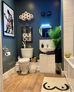 a bathroom with blue walls and white fixtures, including a toilet, sink, mirror, rugs and pictures on the wall