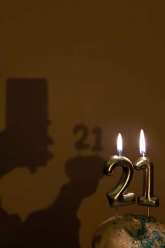 a birthday cake with two candles in the shape of number twenty and an old man's shadow