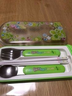 two spoons and a fork in a plastic container on a wooden table next to each other