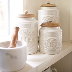 three white canisters sitting on top of a shelf next to a bowl and spoon