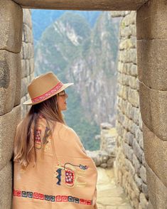 a woman in a hat and ponchy sitting on top of a stone wall