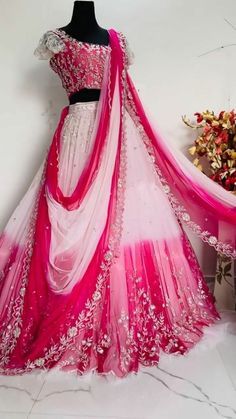 a pink and white lehenga on display in front of a vase with flowers