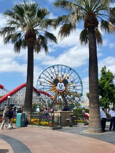 people are walking around in front of palm trees and a ferris wheel at an amusement park