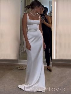 a woman standing in front of a mirror wearing a white dress