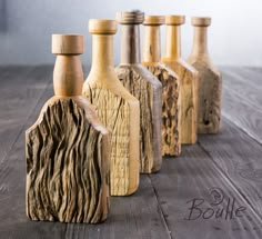 six wooden bottles are lined up on the table, one is carved from wood and the other is made out of driftwood