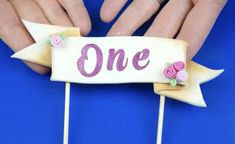 someone is holding a cake topper with the word one on it and two flowers