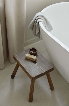 a white bath tub sitting next to a wooden stool with a hair brush on it