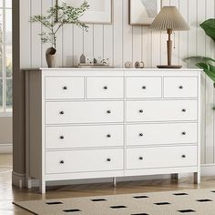 a white dresser sitting in a room next to a lamp and pictures on the wall