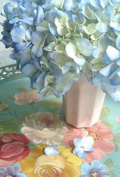 a vase filled with blue and white flowers on top of a colorful tablecloth covered table