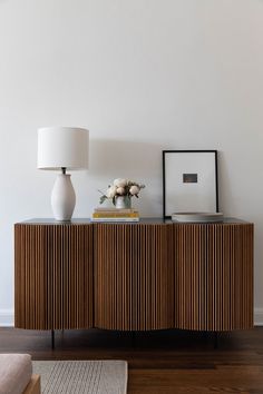 a white vase sitting on top of a wooden cabinet next to a lamp and pictures