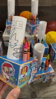 a person holding up a small box with crayons and markers on it's sides