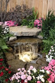 a garden with flowers, rocks and water features an artificial waterfall in the center surrounded by greenery