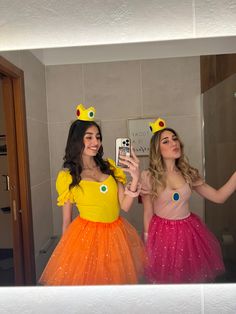 two women in costumes taking a selfie in the mirror with their cell phones,