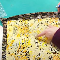 someone is using scissors to cut fabric on a piece of cloth with yellow and black designs